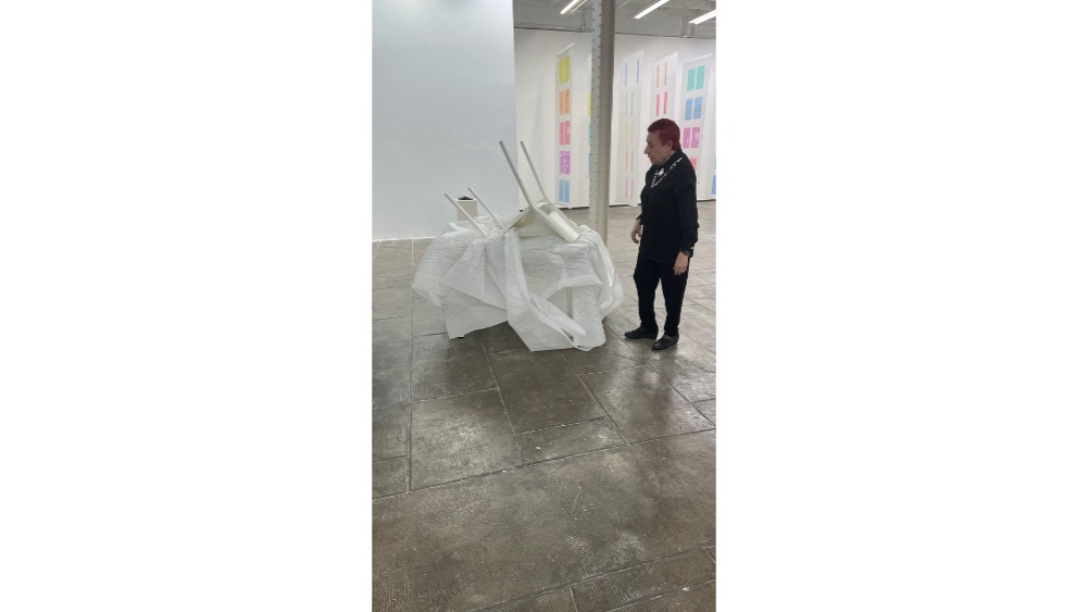 Concha Jerez junto a la obra "INTERVAL ÚNIC DE TEMPS AUTOCENSURAT", 2013-2022. Pieza tridimensional performativa. 1 mesa blanca, 1 silla intervenida con escritos en rotulador permanente, 1 rollo de poliéster de 20 x 1 m.